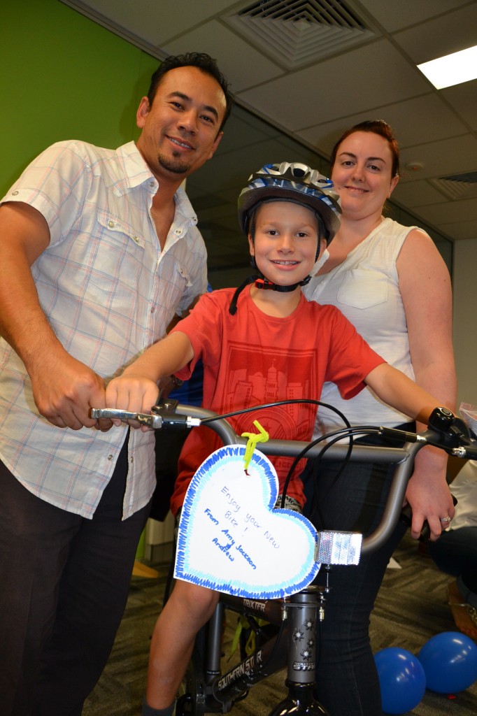 Build a bike for kids charity groups happily sitting on bike built by staff that is rewarding for all! Here a young child in their bright red shirt receives their gifted and corporate donated BMX stunt bikes.